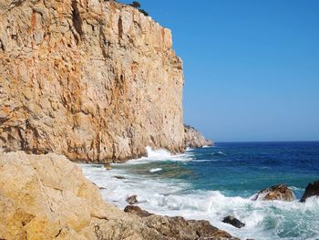 Scenic view of rocks on beach against clear blue sky