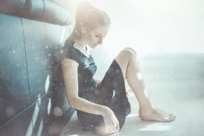 Full length of thoughtful beautiful woman sitting on carpet