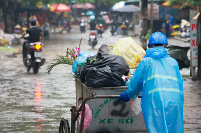 Rear view of people walking on street in city during rainy season