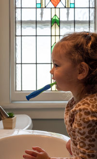 Side view of girl brushing teeth at home