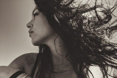 Low angle view of young woman looking away while sitting against sky