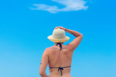 Rear view of bikini woman wearing hat against blue sky