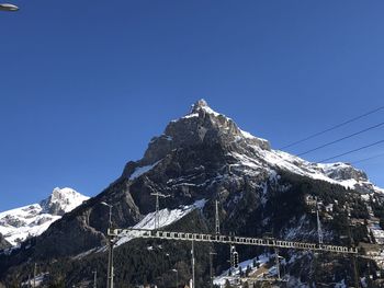 Low angle view of snowcapped mountain against clear blue sky