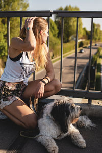 Young woman with dog sitting by railing on footbridge