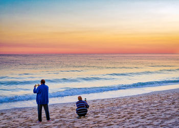 Rear view of men on shore at beach during sunset