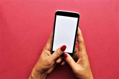 Close-up of hand holding mobile phone against red background