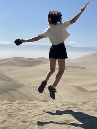 Rear view of girl jumping at desert against sky