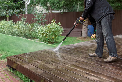 Man cleaning walls and floor with high pressure power washer. washing terrace wood planks and 