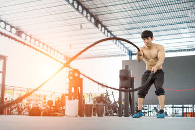 Muscular man exercising with rope in gym