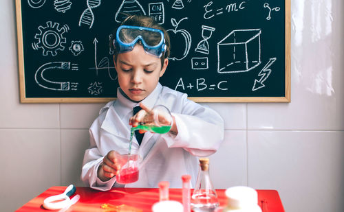Boy wearing lab coat while mixing chemicals in classroom
