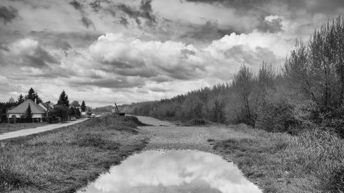 Dirt road passing through field against cloudy sky