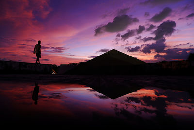 Silhouette person by lake against sky during sunset