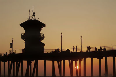 Silhouette people on lighthouse by sea against clear sky during sunset