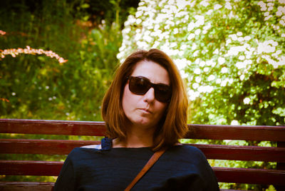 Portrait of woman wearing sunglasses while sitting on bench at park