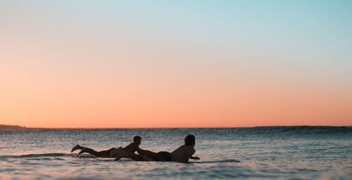 Silhouette men in sea against clear sky during sunset