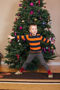 Smiling boy with arms outstretched standing against christmas tree at home