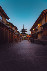 Illuminated street amidst buildings against sky at dusk