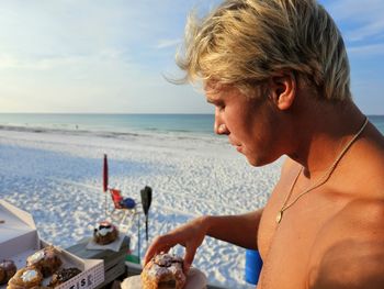 Suntanning millennial man at florida beach eating a doughnut.
