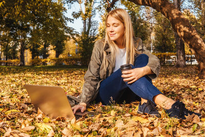 Woman using laptop while sitting on leaves in park