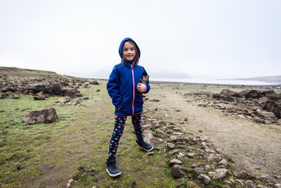 Portrait of smiling girl standing on field against sky