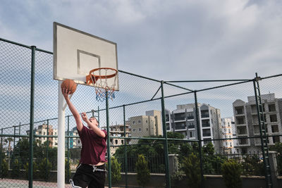 Man playing basketball hoop against sky in city