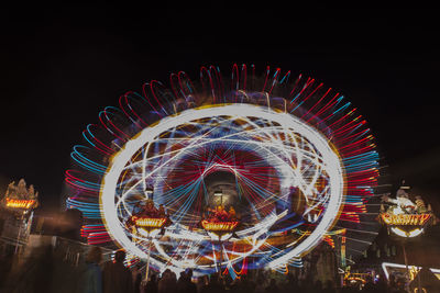 Low angle view of people by illuminated amusement park rides against sky at night