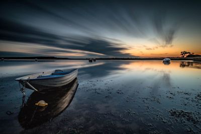 Boats moored at beach against sky during sunset