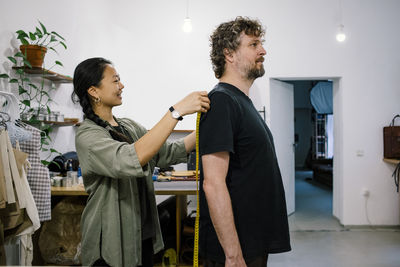 Female tailor taking measurement of male customer while standing at store