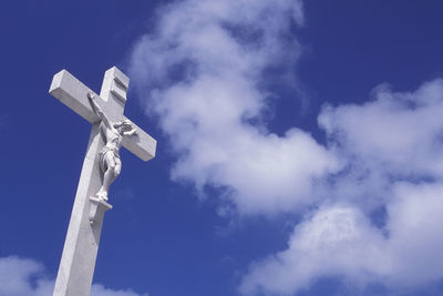 Low angle view of white cross against blue sky