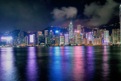 Illuminated buildings by river against sky at night