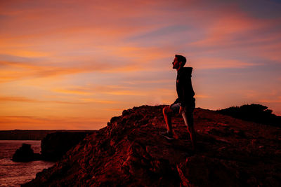 Man standing on rock against sky during sunset