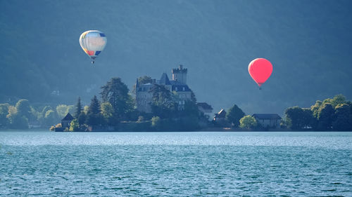 Lac d'annecy - château de duingt - hot air balloons flying over lake against sky during sunset