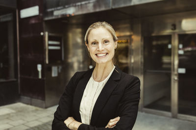 Portrait of confident female entrepreneur with arms crossed standing against building