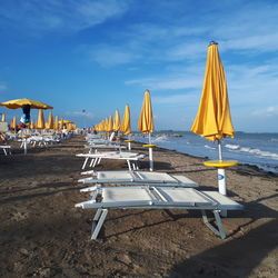 Lounge chairs and parasols on beach against sky