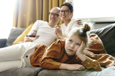 Unhappy daughter watching movie with parents at home