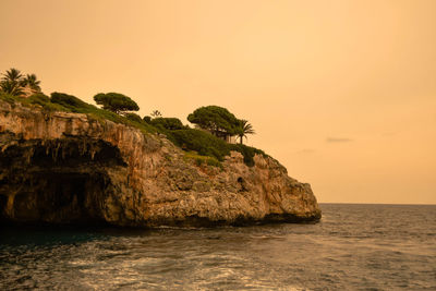 Rock formation in sea against clear sky during sunset