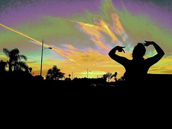 Silhouette man with arms raised against sky during sunset