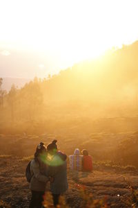 Rear view of people walking on land against sky during sunset