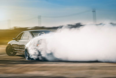 Blurred motion of car emitting smoke against sky