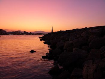 Silhouette rocks by sea against sky during sunset