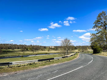 Empty road by trees against blue sky