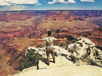 Full length rear view of man standing on rock with arms outstretched at grand canyon national park