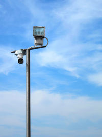 Low angle view of security camera and light against sky