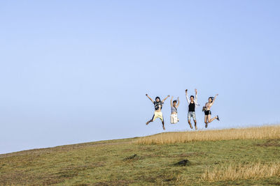 People jumping on field against clear sky