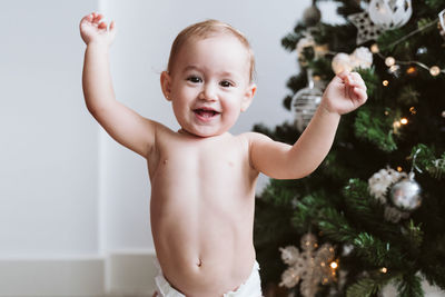 Happy baby girl wearing diaper decorating christmas tree