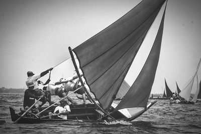 Men in sailboat racing on sea against sky