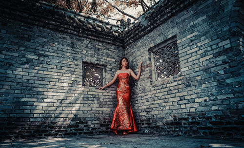 Portrait of young woman standing against brick wall