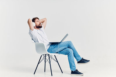 Full length of man sitting on chair against white background