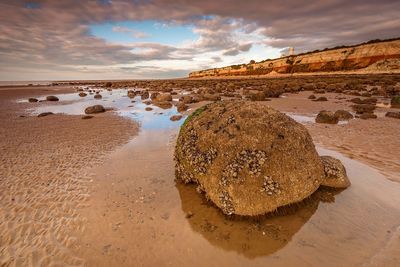 View of rocks at beach against cloudy sky