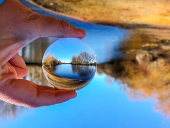 Close-up of hand holding crystal ball against trees